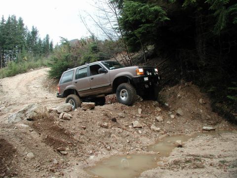 Lifted tan SUV on a muddy, rocky off-road trail.