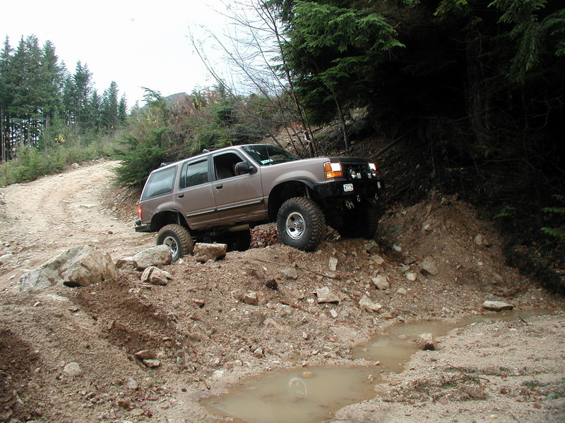 Lifted tan SUV on a muddy, rocky off-road trail.