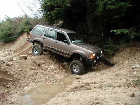 Lifted brown Ford Explorer off-roading on a muddy, rocky trail.