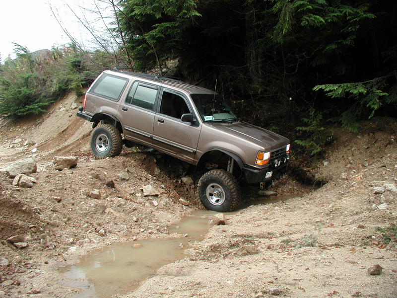 Lifted brown Ford Explorer off-roading on a muddy, rocky trail.