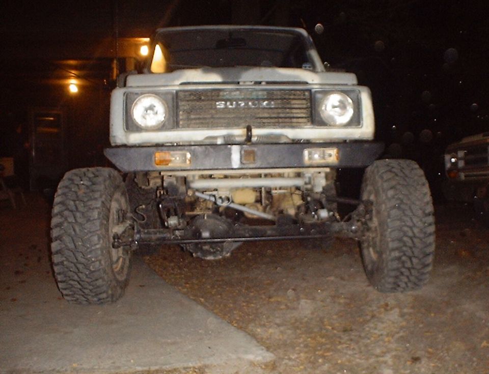 Suzuki Samurai with aftermarket bumper and large tires, front view. Another vehicle is parked to the right