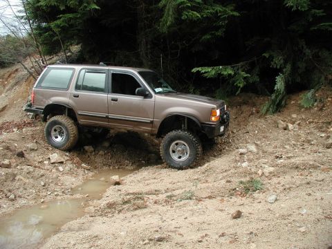 Lifted tan 4-door SUV off-roading on a muddy trail.