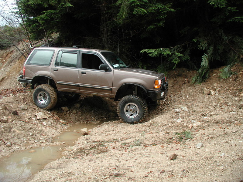 Lifted tan 4-door SUV off-roading on a muddy trail.