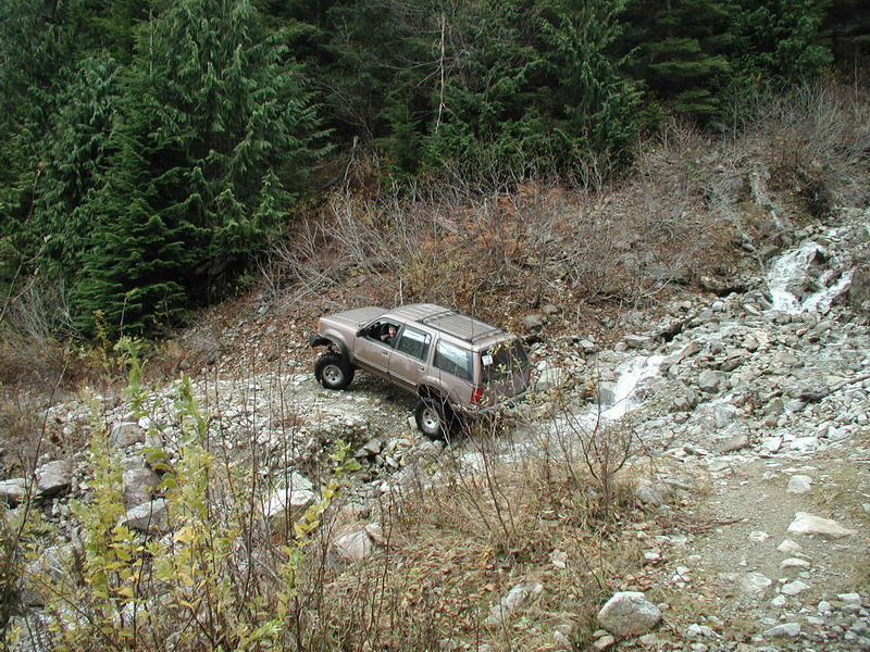 Lifted tan SUV driving on a rocky off-road trail next to a stream.