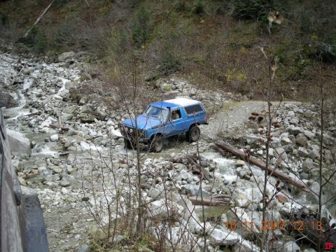 1985 Ford Bronco driving through a rocky stream.