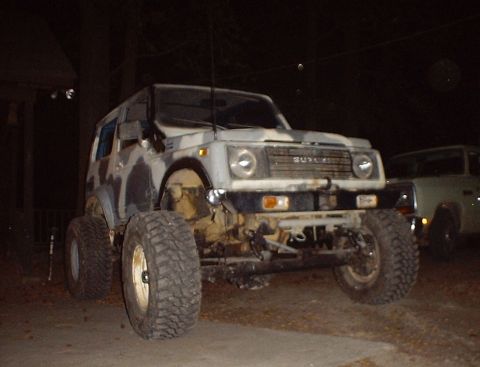 1989 Ford Bronco - A Suzuki Samurai with custom paint and oversized tires is parked outdoors at night.