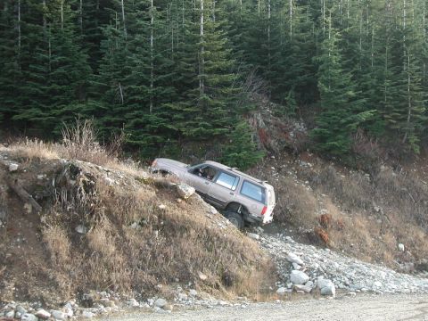 Tan SUV on a steep, rocky off-road trail with a forest.