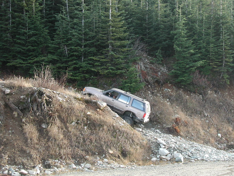 Tan SUV on a steep, rocky off-road trail with a forest.
