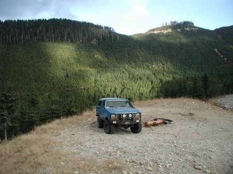 Blue Ford Bronco parked on a clearing with a mountain forest background.