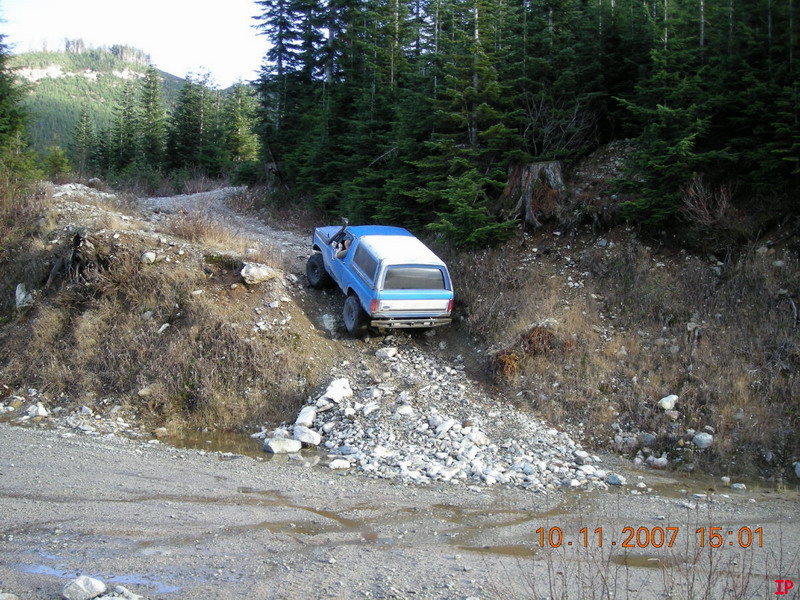 Blue Ford Bronco off-roading on a rocky trail with trees.