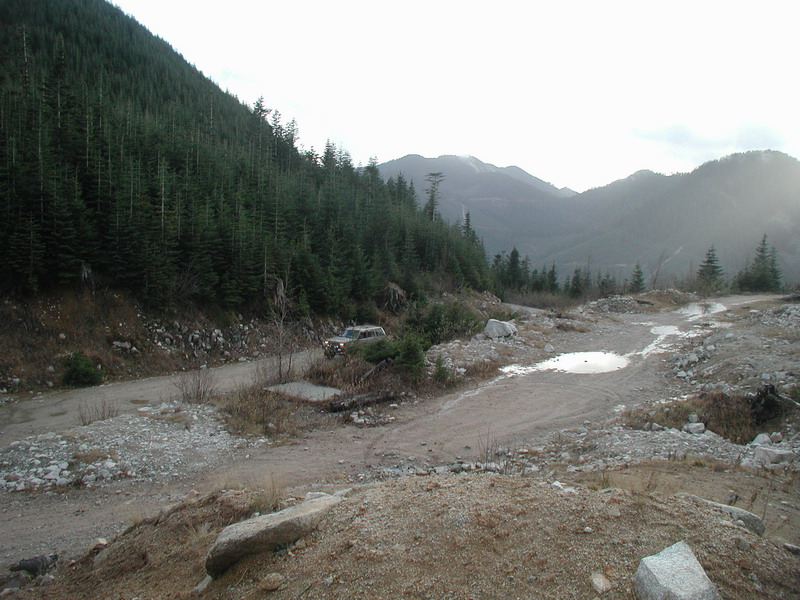 Tan SUV on a dirt road in a forest with mountains in the background.