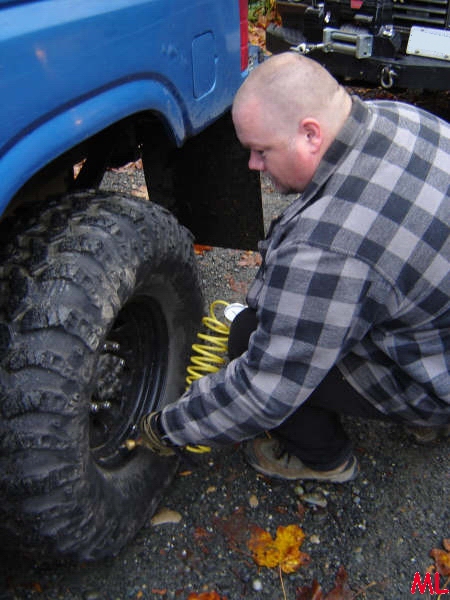 Man inflating a large off-road tire on a blue vehicle