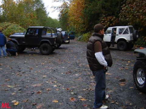 Black Jeep Wrangler parked on a gravel lot with people and other vehicles.