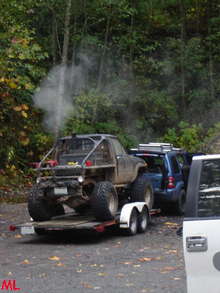 Modified off-road truck on a trailer with a blue SUV behind it.