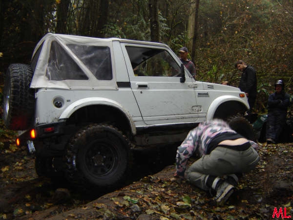 White Suzuki Samurai soft top off-roading with people around.