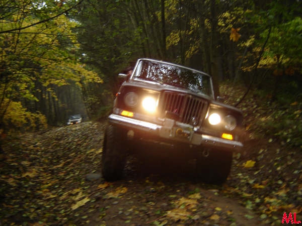 Dark Jeep Cherokee driving on a dirt path in a forest during autumn.