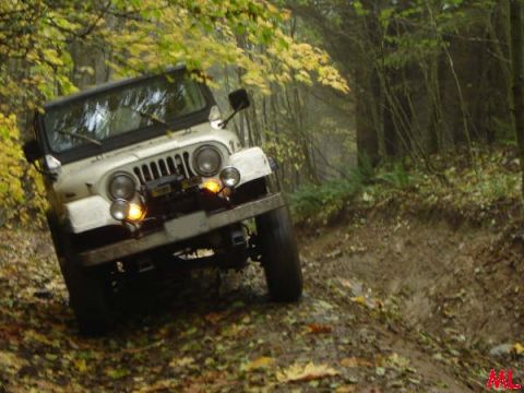 White Jeep Wrangler driving on a muddy forest trail in autumn.