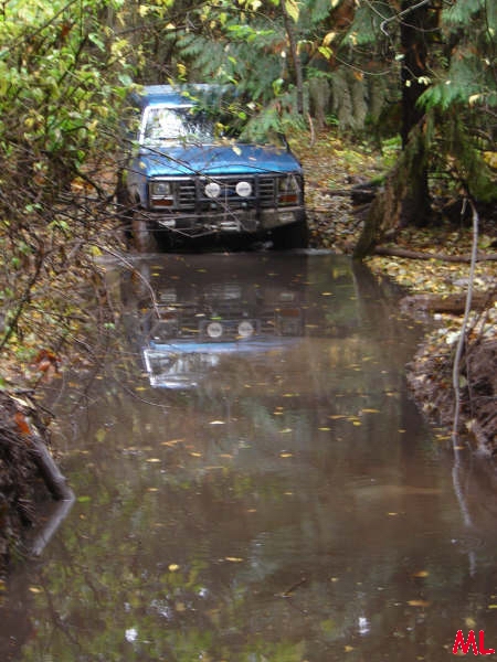 Blue SUV driving through a muddy path in a forest.