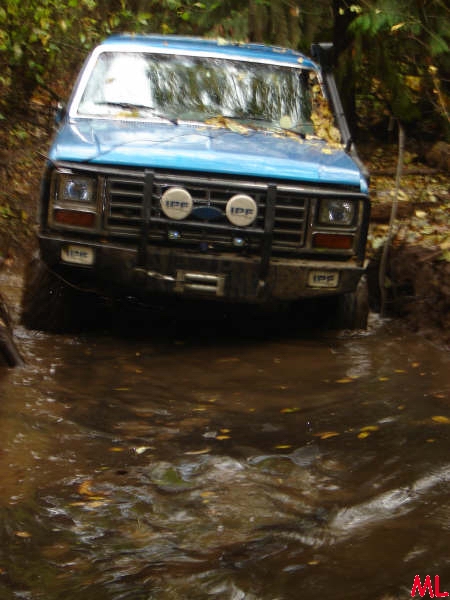 Blue off-road vehicle driving through a muddy stream in a forest.