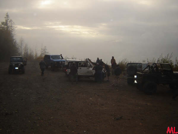 Off-road vehicles on a dirt road with people gathered around a white SUV.