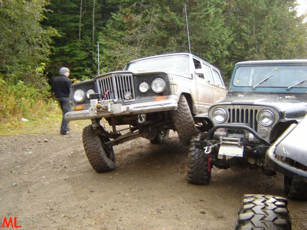 Two off-road Jeeps parked on a dirt road in a forest.