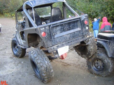 Rear 3/4 view of a black, lifted Jeep Wrangler on a dirt road.