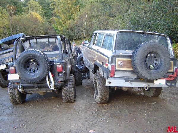 Rear view of two off-road vehicles, one a wood-paneled SUV with a spare tire.