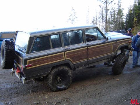 Lifted Jeep Grand Wagoneer with wood paneling on dirt road, spare tire on rear.