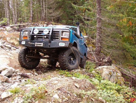 Blue Ford Bronco on a rocky trail with trees.