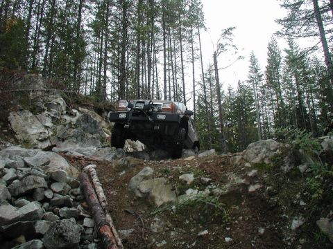 1985 Ford Bronco on a rocky, wooded trail, angled upwards.