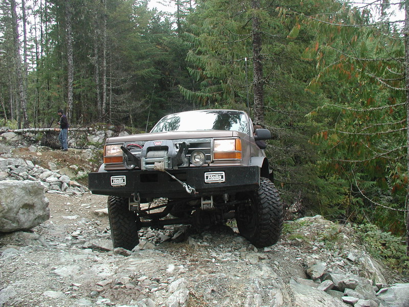 Brown off-road SUV with winch and custom bumper on a rocky trail.