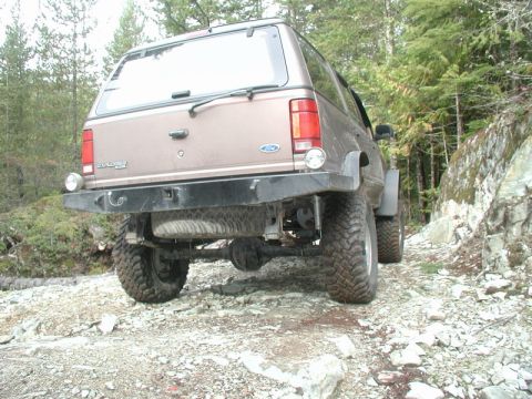 Rear view of a lifted tan Ford Explorer SUV on a rocky off-road trail.