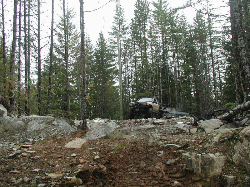 Two off-road vehicles on a rocky trail in a forest.