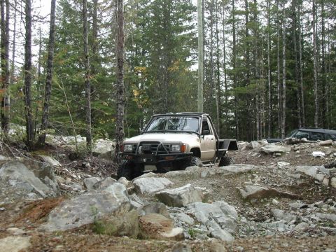 Modified beige pickup truck on a rocky off-road trail.