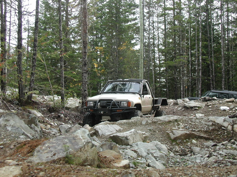 Modified beige pickup truck on a rocky off-road trail.