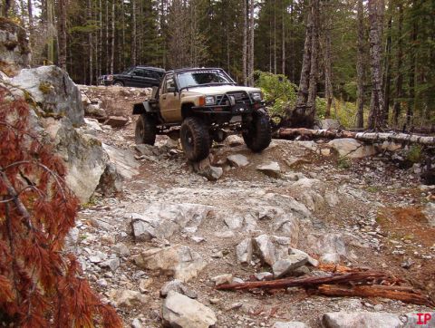 Lifted tan Toyota pickup truck on a rocky, wooded trail.