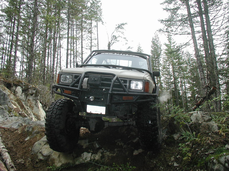 Tan off-road pickup truck with custom bumper and large tires on a rocky trail.