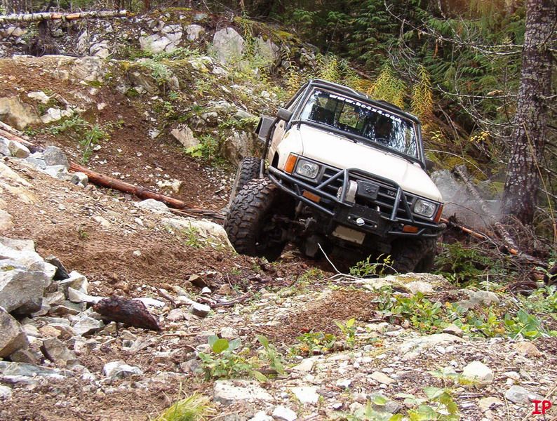 Tan off-road vehicle with brush guard climbing a steep, rocky trail.