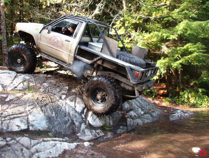 Modified pickup truck with large tires climbing a rocky terrain.