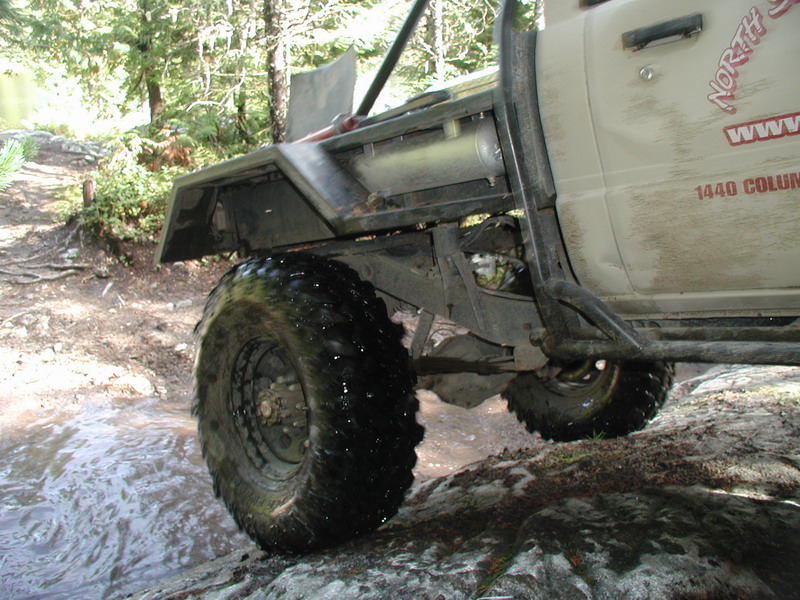 Modified off-road pickup truck driving through a muddy puddle on a rocky trail.