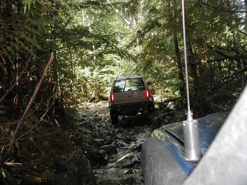 Two SUVs driving on a rocky, wooded trail.