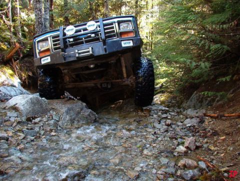 1985 Ford Bronco navigating a rocky stream in a forest.