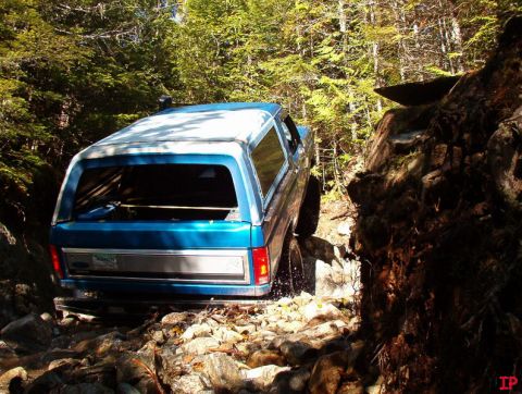 Blue Ford Bronco off-roading on a rocky, wooded trail.