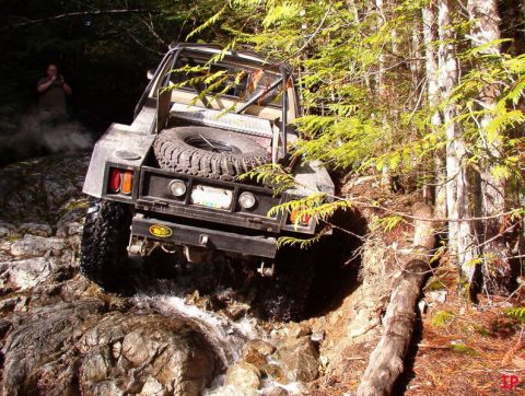 Off-road pickup truck driving through a rocky stream in a forest.