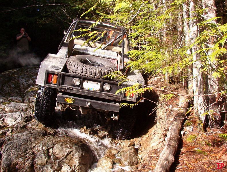 Off-road pickup truck driving through a rocky stream in a forest.