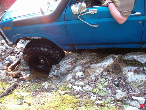 Blue Ford Bronco off-roading over rocks, front passenger tire stuck in mud and rocks.