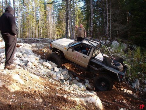 Tan Toyota pickup truck with roll cage on a rocky trail, driver waving.