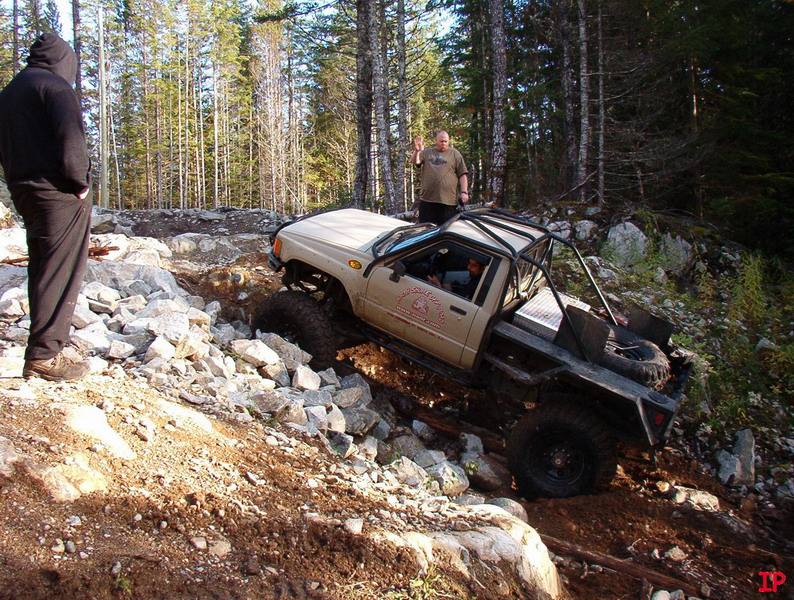 Tan Toyota pickup truck with roll cage on a rocky trail, driver waving.