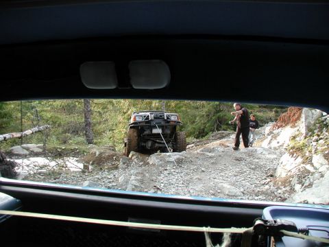Off-road SUV being winched up a rocky hill by two people.