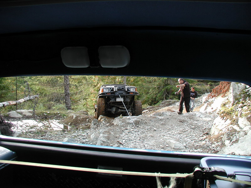 Off-road SUV being winched up a rocky hill by two people.
